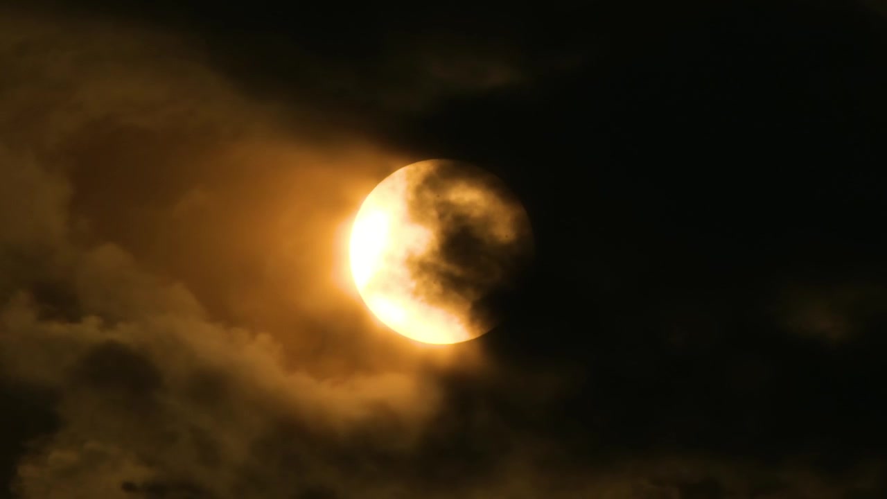 Close up, Dark rolling clouds reveal a bright orange sun before setting.