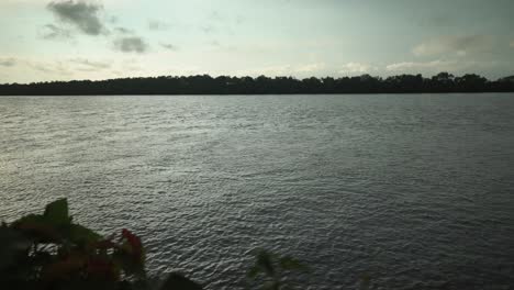 Water-calmly-flowing-slowly-in-a-lake-with-soft-wind-blowing-and-the-leaves-of-the-trees-at-the-banks-swaying-in-it