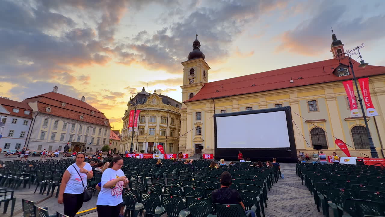 Sibiu, Romania, 17 July 2025: Red TIFF installation on Sibiu Main Square at dusk. Historic Brukenthal Palace and church tower frame a lively film festival