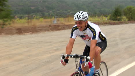 a bicyclist smiles as he peddles along a highway in a rural area