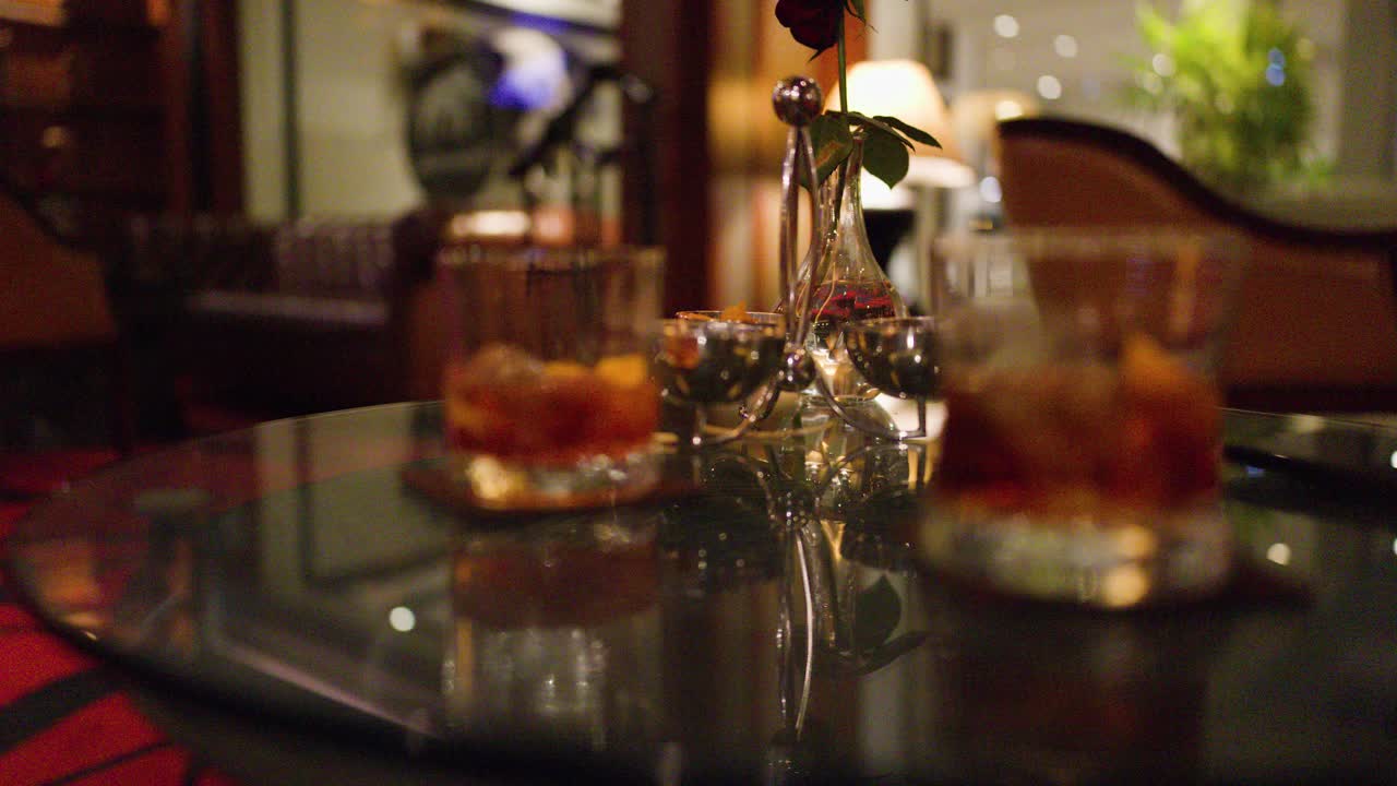 Two whiskey glasses with ice on reflective bar table, warm lighting, shallow depth of field