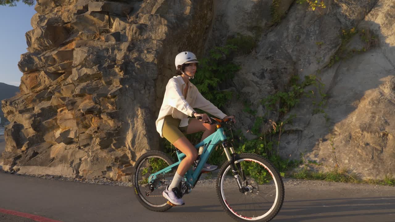 Sporty Girl Wearing Helmet While Riding Bicycle Over Road Through Rock Cliffs