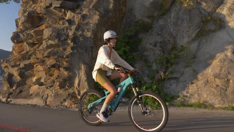 menina esportiva usando capacete enquanto anda de bicicleta pela estrada através de penhascos rochosos