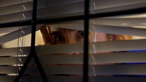 a paranoid scared woman looking through blinds at home