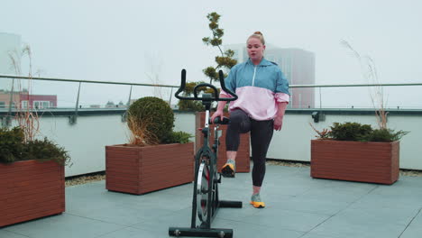 Athletic-woman-riding-on-spinning-stationary-bike-training-routine-on-house-rooftop,-weight-loss