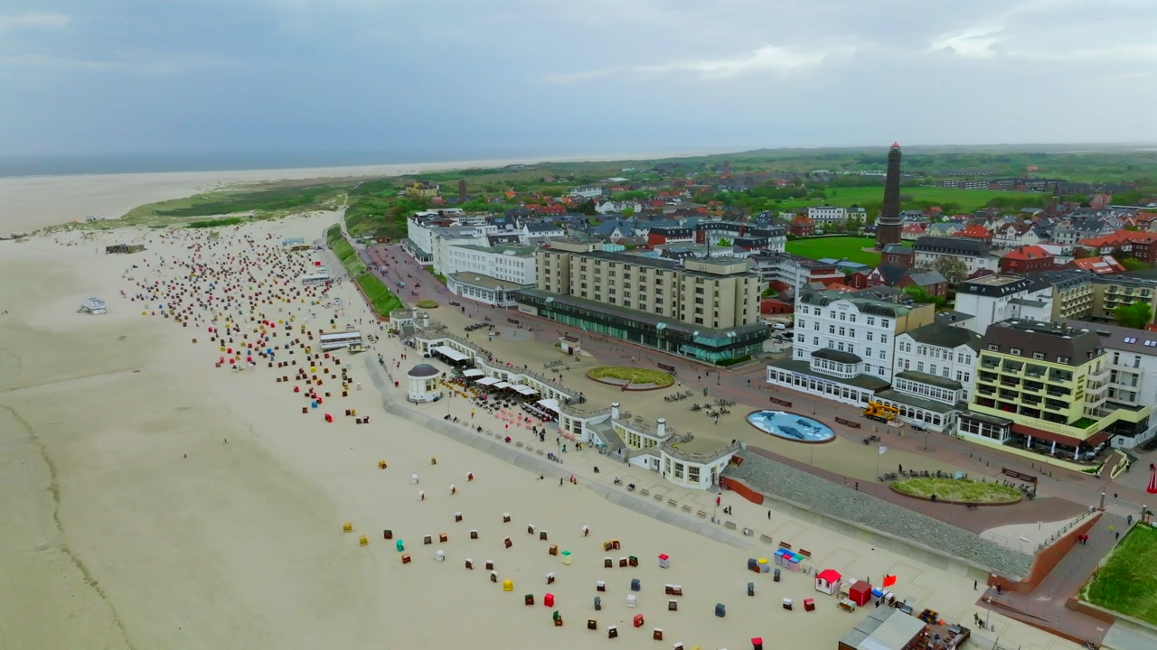 Beachfront promenade with rows of colorful strandkorb beach chairs in front of historic spa hotels and buildings along the sandy coast of Borkum