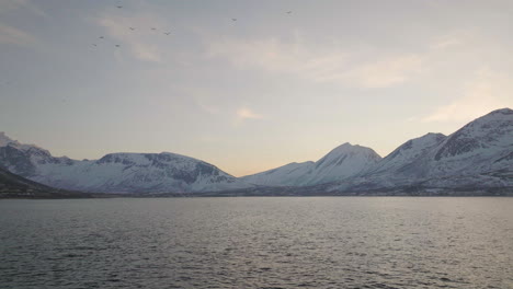 Aerial-over-open-arctic-ocean,-view-of-snowy-mountains-on-mainland