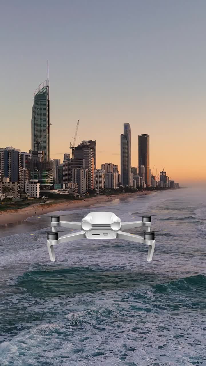 En drone flyver elegant over havets bølger mod en bysilhuet under en fredfyldt solnedgang og fanger dynamiske luftbilleder.