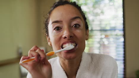 Portrait-of-biracial-woman-in-robe-brushing-teeth