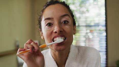 portrait of biracial woman in robe brushing teeth