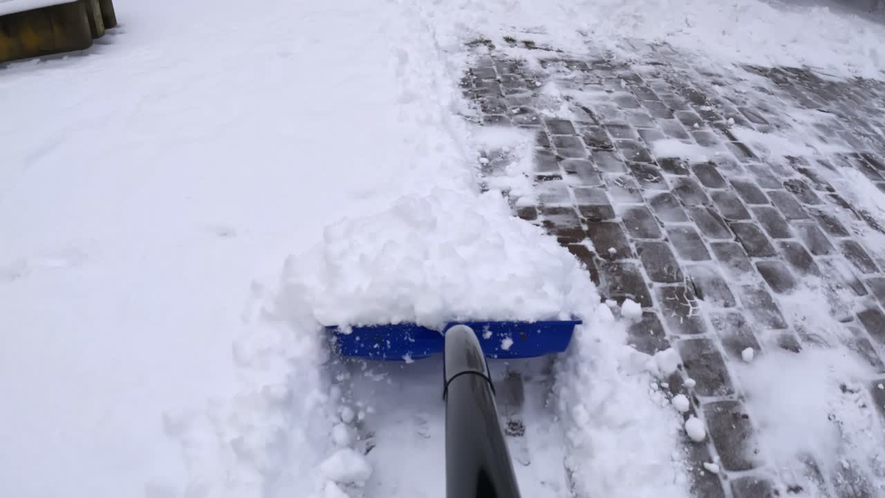 POV pushing a blue snow shovel along cobblestone pavers, cutting a clean edge and moving powder aside to clear a safe walkway during winter driveway maintenance