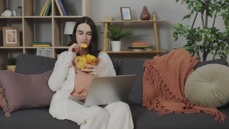woman eating chips while watching laptop
