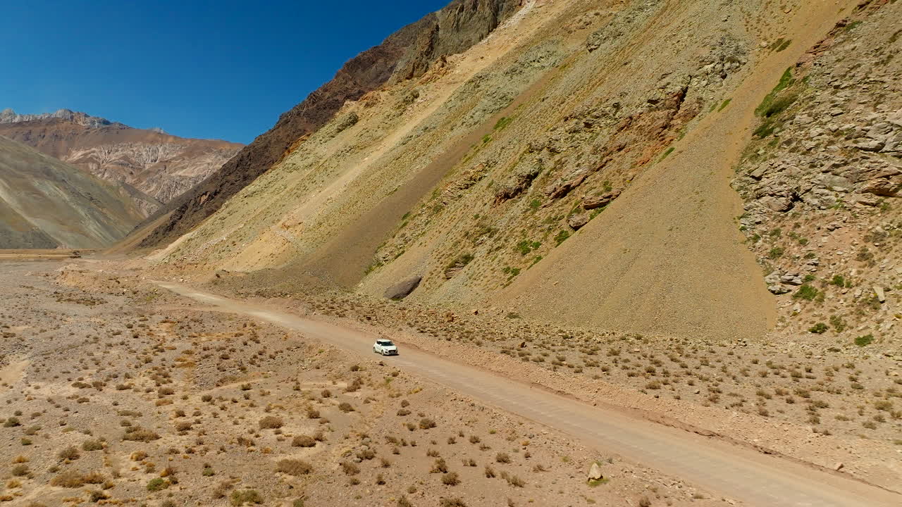 Aerial view of white rental car driving on dirt road of rugged Cajon del Maipo