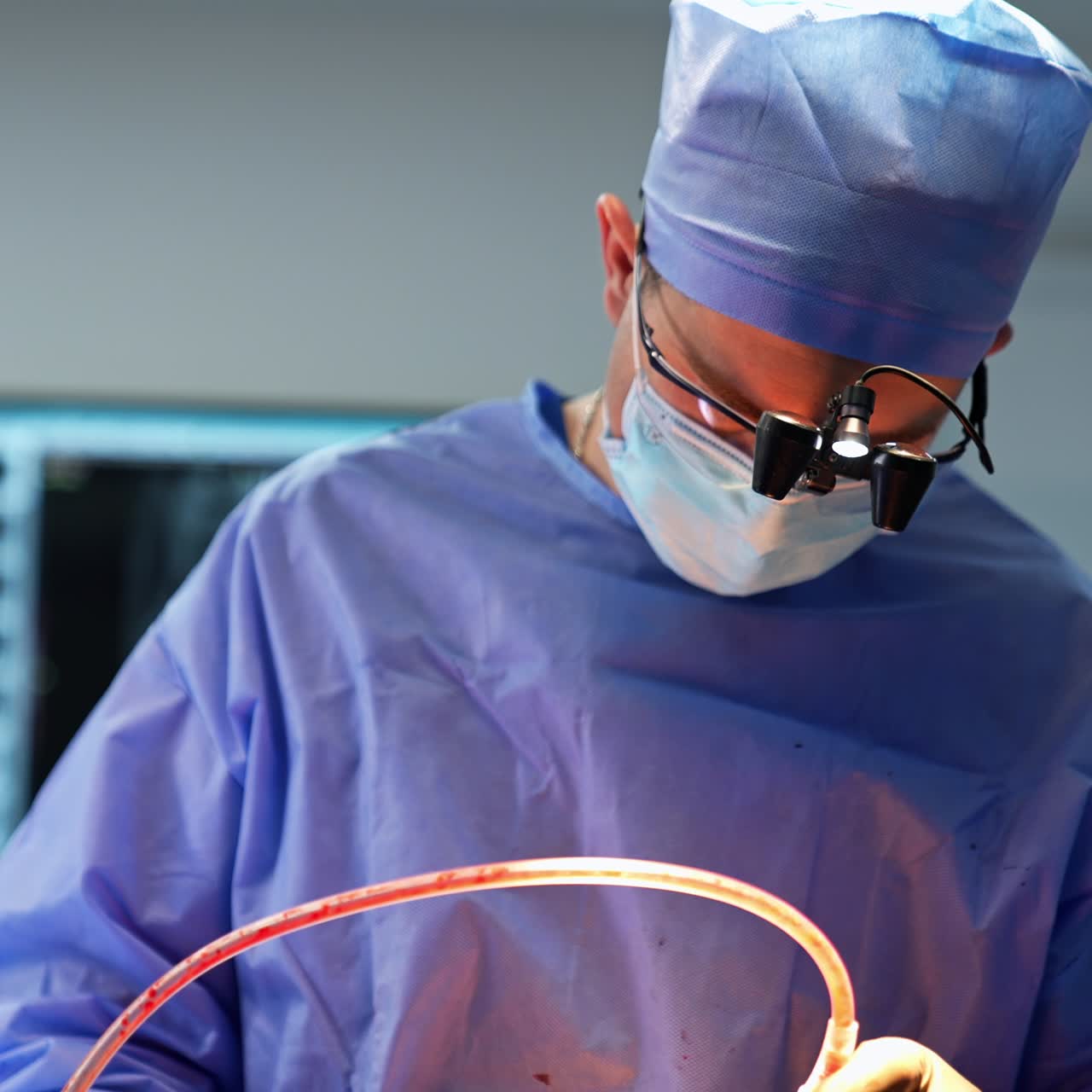 Mid-aged doctor wearing device glasses on his head bent over the patient. Surgeon using tool with tube at operation. Close up portrait with gradual distancing
