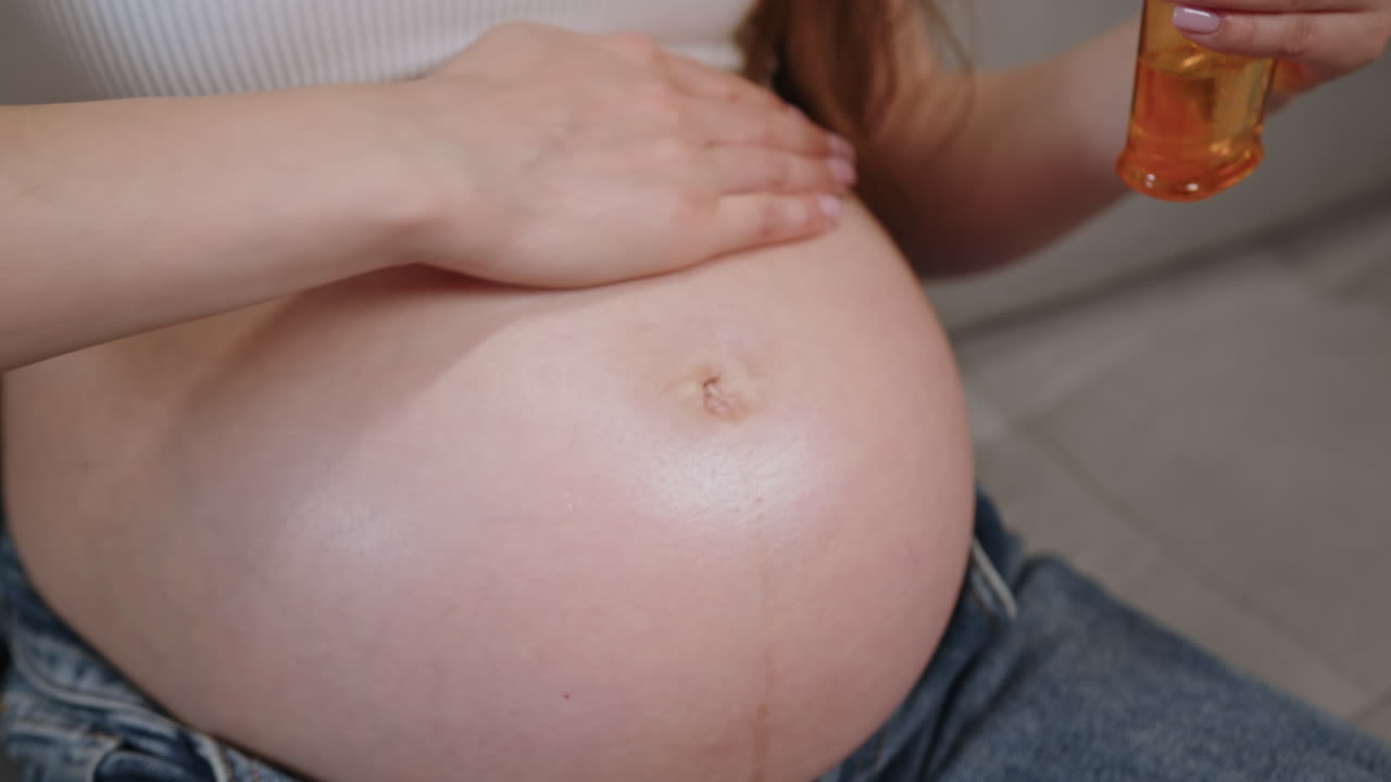 Una donna applica dell'olio sul suo ventre durante la gravidanza per idratare la pelle e prevenire le smagliature