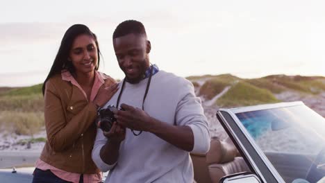 african american couple using digital camera to take pictures while standing near the convertible ca