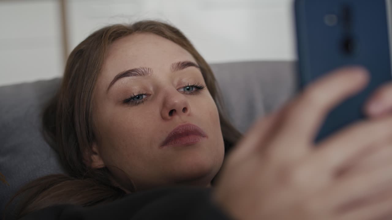 mujer caucásica acostada en el sofá y usando el teléfono móvil.