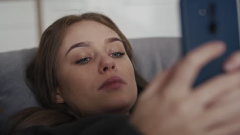 caucasian woman lying down on the couch and using mobile phone.