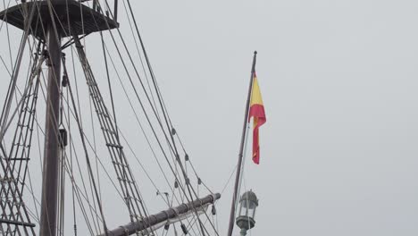 Galleon-Andalucia-replica-ship-detail-steady-shot-of-spanish-flag-at-the-poop-deck-mast-and-sail-while-docked-in-Valencia-in-slow-motion-60fps