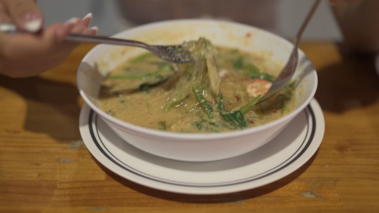 Asian woman eating famous Thai Suki noodles soup with shrimps in restaurant close-up shot