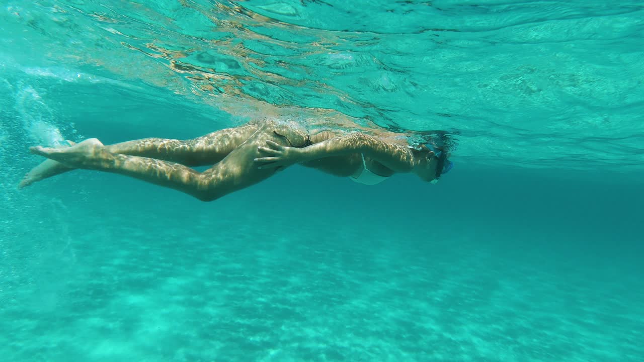 Giovane donna che fa snorkeling in un mare blu cristallino, ripresa laterale subacquea