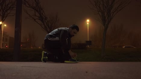 runner ties his shoelaces in a spots track at night time