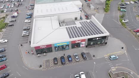 aerial view of a bustling retail park featuring various shops, a large parking lot filled with cars, and solar panels on the roof