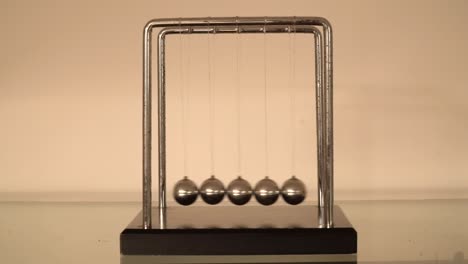 Newton's-cradle-over-cream-background,-balls-swinging-FRONT-VIEW