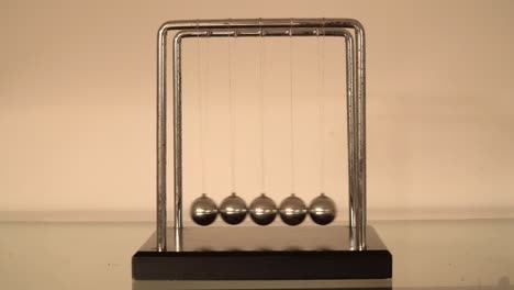 newton's cradle over cream background, balls swinging front view