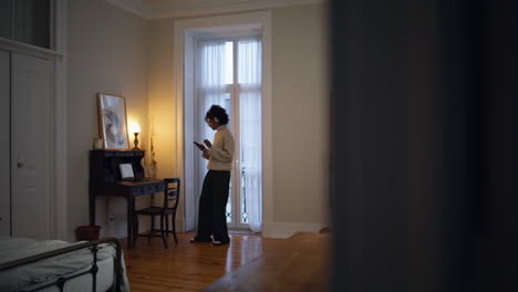 relaxed lady using phone in evening room. headphones curly woman changing music