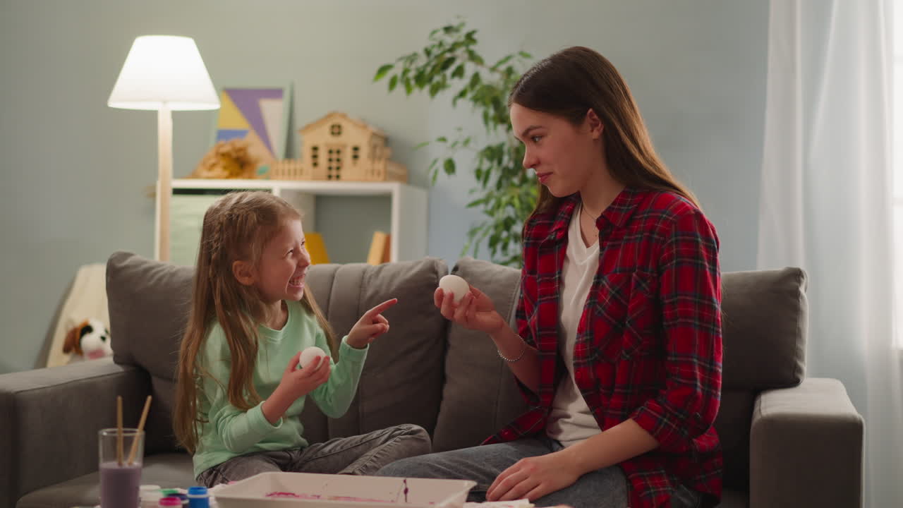 la niña se ríe y señala a la hermana con el huevo de pascua