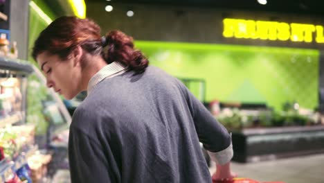 Young beautiful brunette girl in her 20&#039;s trying to choose prepacked salad leaves in a grocery store.