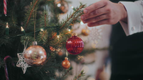 mano colgando bauble rojo en el árbol de navidad en casa