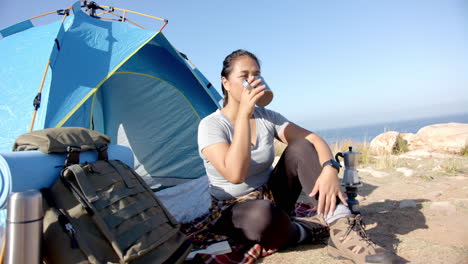 camping by tent, woman drinking coffee and relaxing after mountain hike