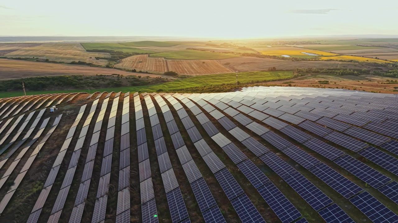 Solpaneler dækker et stort felt i et landområde under solnedgang, fremhæver installationer for vedvarende energi med et bredt landskab i baggrunden