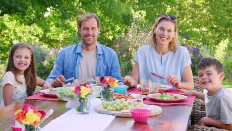padres y niños almorzando en el jardín miran a la cámara