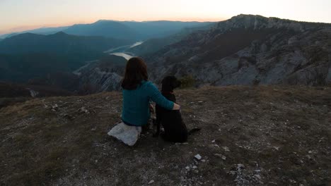 girl sitting and cudling black labrador dog on a mountain