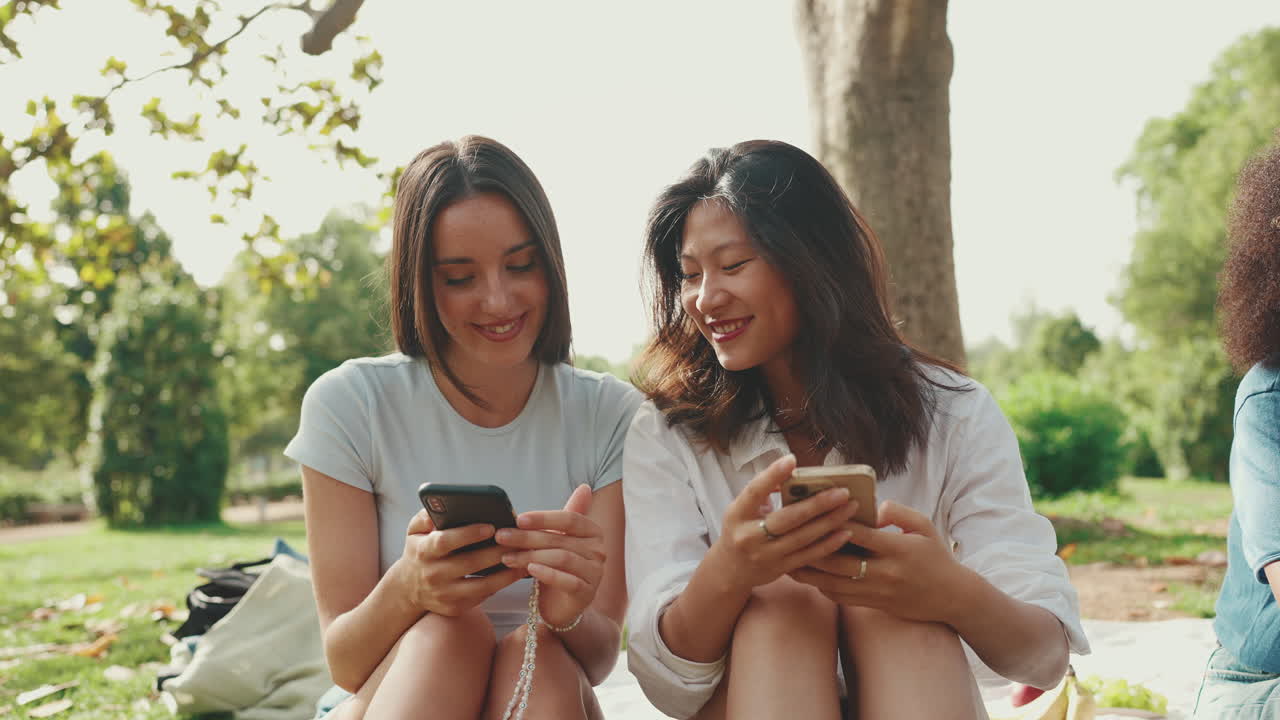 Two women using their phones in the park