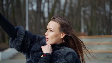 beautiful woman doing selfie on her mobile phone. side view portrait of a nice girl photographing herself on cellphone outdoors. slow motion.