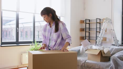 Women-with-Adhesive-Tape-Packing-Boxes-at-Home.moving,-people-and-real-estate-concept--women-with-adhesive-tape-packing-boxes-at-home