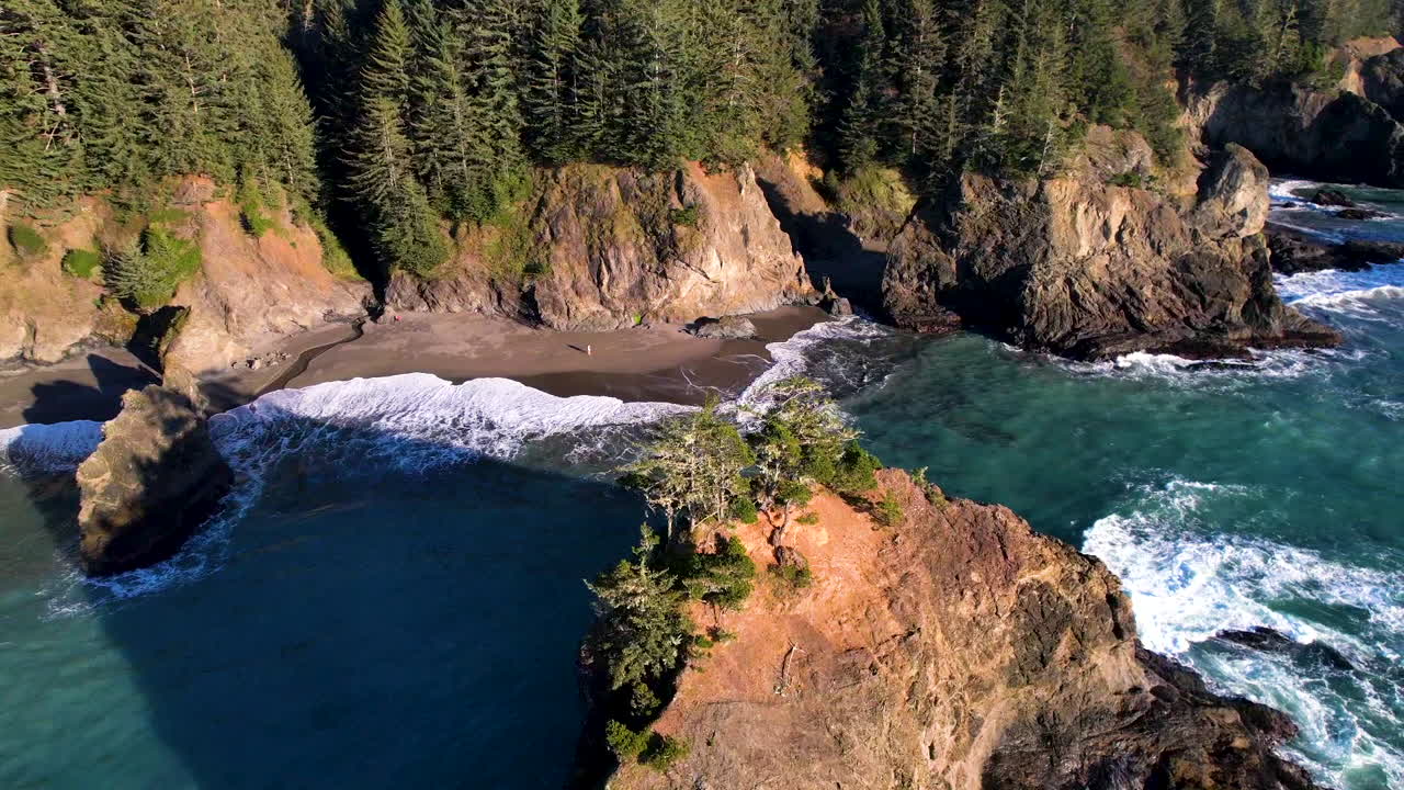 A drone rotating around a large sea stack with the ocean, cliffs and a secluded beach around.