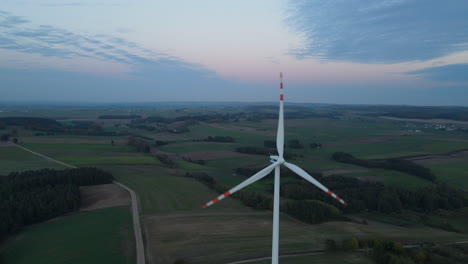 Rotating-wind-turbine-on-farmland-field-with-wide-landscape-and-colorful-clouds-in-background