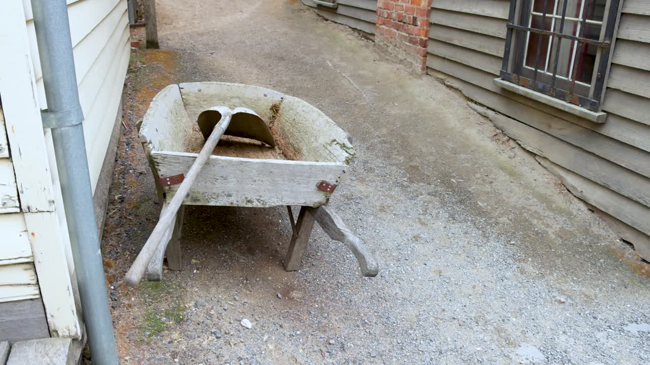 A wheelbarrow rests in a narrow alley between wooden buildings in Sovereign Hill, Melbourne. Overcast lighting creates a calm atmosphere