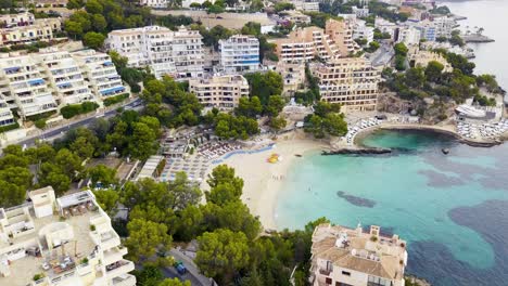 playa illetas with clear waters, beach-goers, and surrounding buildings on a sunny day, drone shot, aerial view