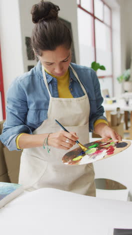 video vertical de una artista femenina biracial pintando en el estudio