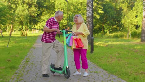 senior stylish couple grandmother, grandfather after shopping with bags using scooter for riding