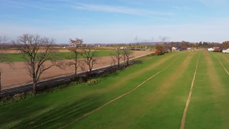 an aerial view of a single rail road track going thru country farmlands as a steam train approaches in the distance on a sunny fall