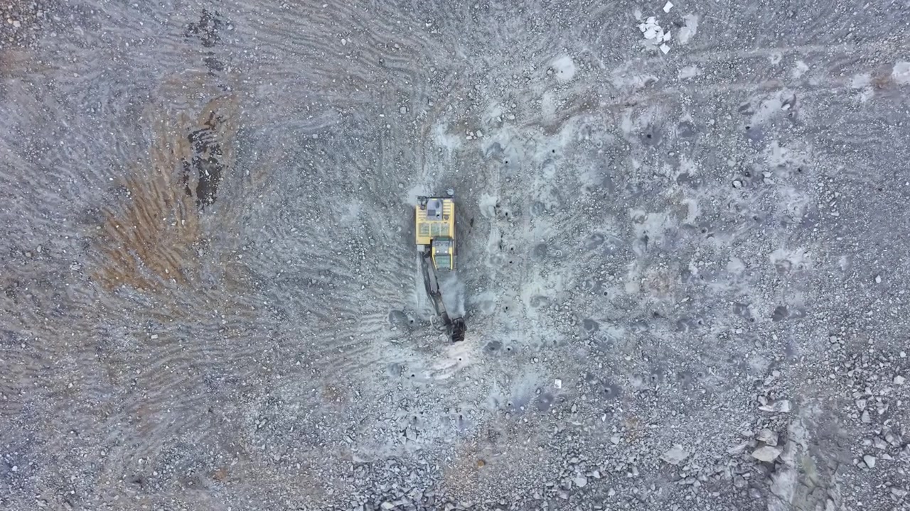 Un mezzo da cantiere opera su una superficie rocciosa per preparare il terreno per un nuovo progetto in un'area mineraria durante le ore diurne.
