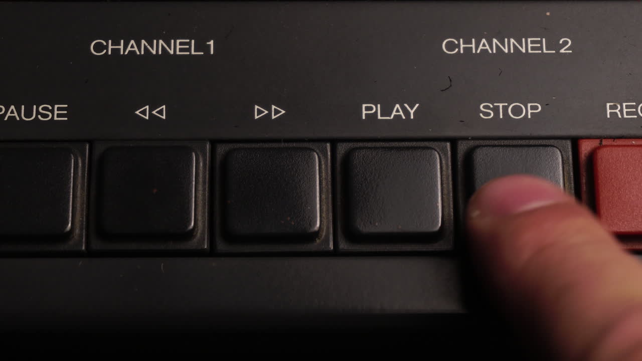 Close-up of a finger pressing the play button on an old audio or video control panel