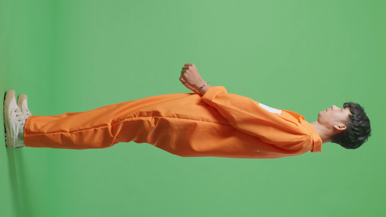 녹색 스크린 배경에 서서 화를 내며 카메라를 쳐다보는 수갑을 입은 아시아 남성 죄수